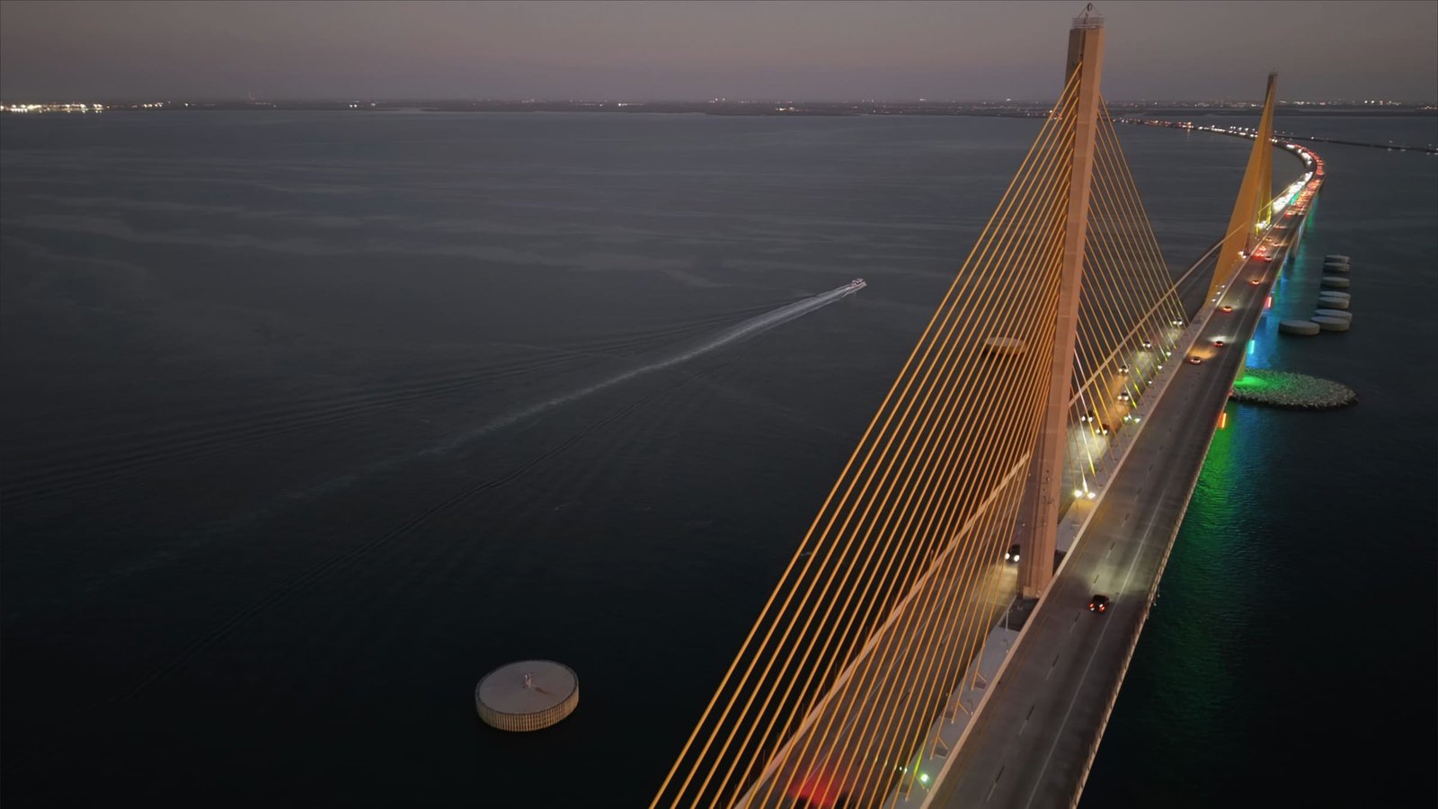 The Sunshine Skyway Bridge over Tampa Bay at twilight, a boat trailing a wake across the dark water