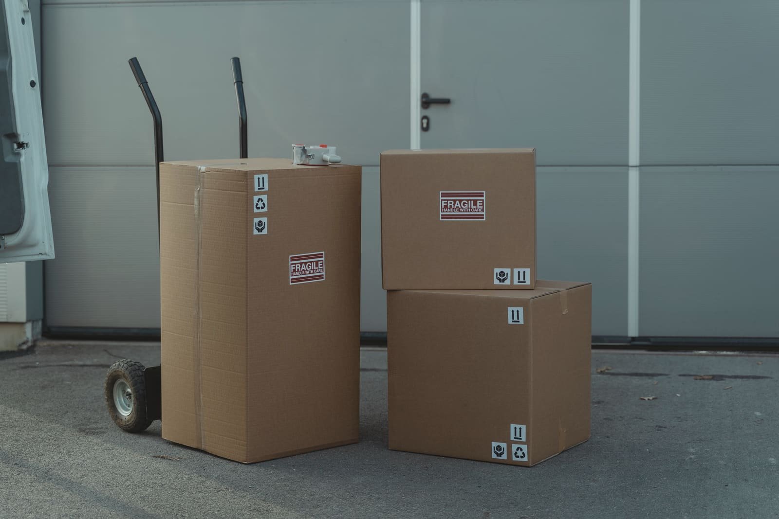 Sealed cartons marked fragile beside a hand truck at a loading door, waiting for pickup