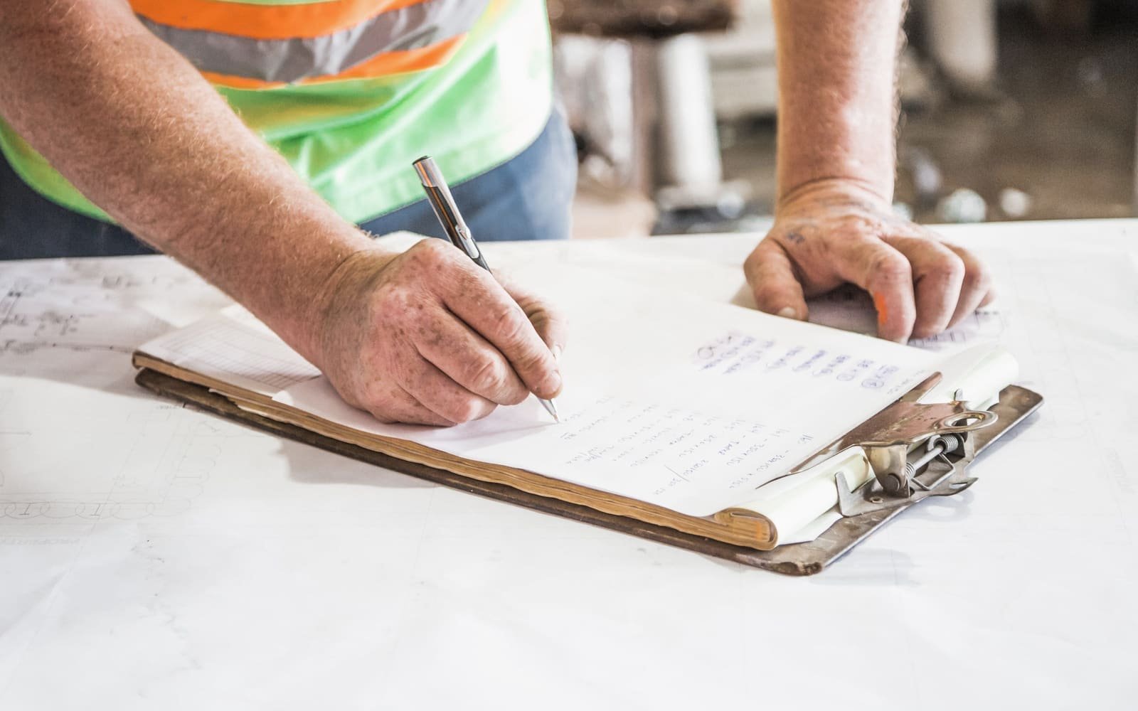 A worker writing on a clipboard laid over construction drawings